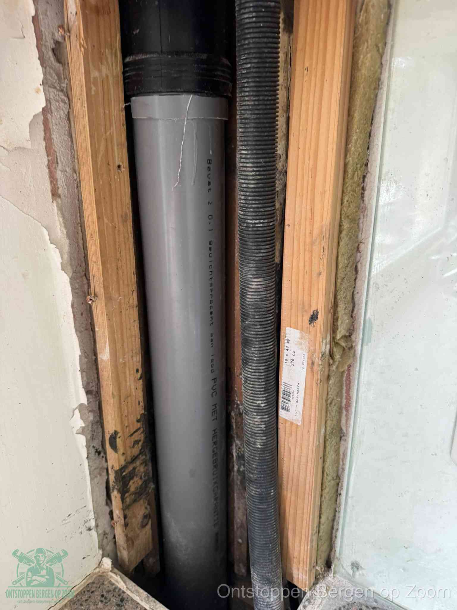 Een grijze PVC-afvoerbuis met een flexibele ribbelslang in een open wandconstructie, een verwaarloosde afvoer die te lang is blijven zitten in Bergen op Zoom