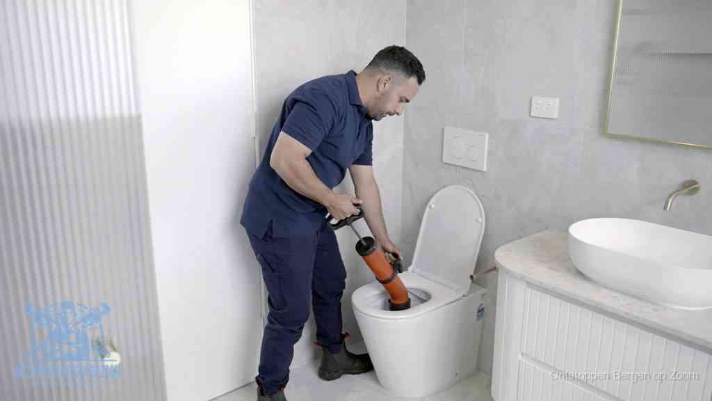 Een monteur buigt over een wandcloset en duwt met de hand een persluchtontstopper in de toiletpot om de verstopping handmatig los te maken in Bergen op Zoom