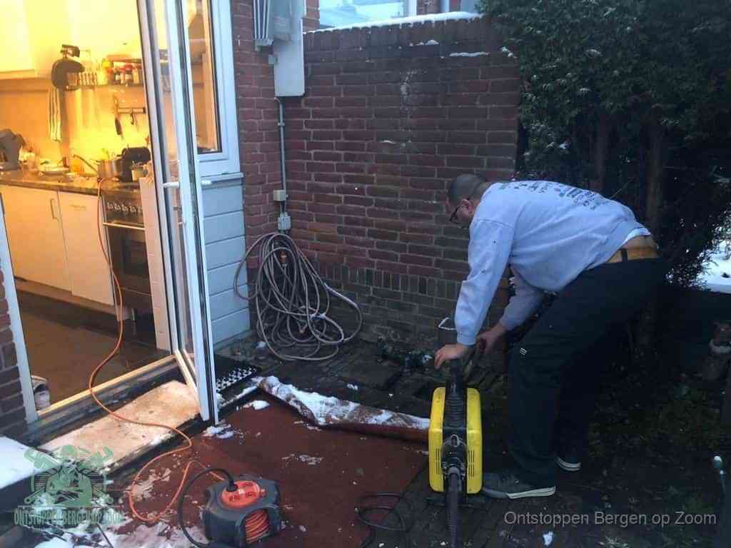 Een monteur werkt buiten bij een open riool-/grondput met een elektrische ontstoppingsmachine om een verborgen afvoerprobleem op te sporen in Bergen op Zoom