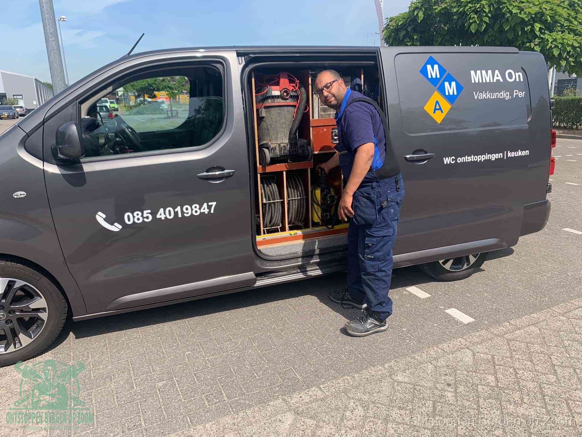 Een monteur bij de open schuifdeur van zijn bedrijfsbus op een parkeerplaats, klaar om de oorzaak van terugkerende afvoerverstoppingen aan te pakken in Bergen op Zoom