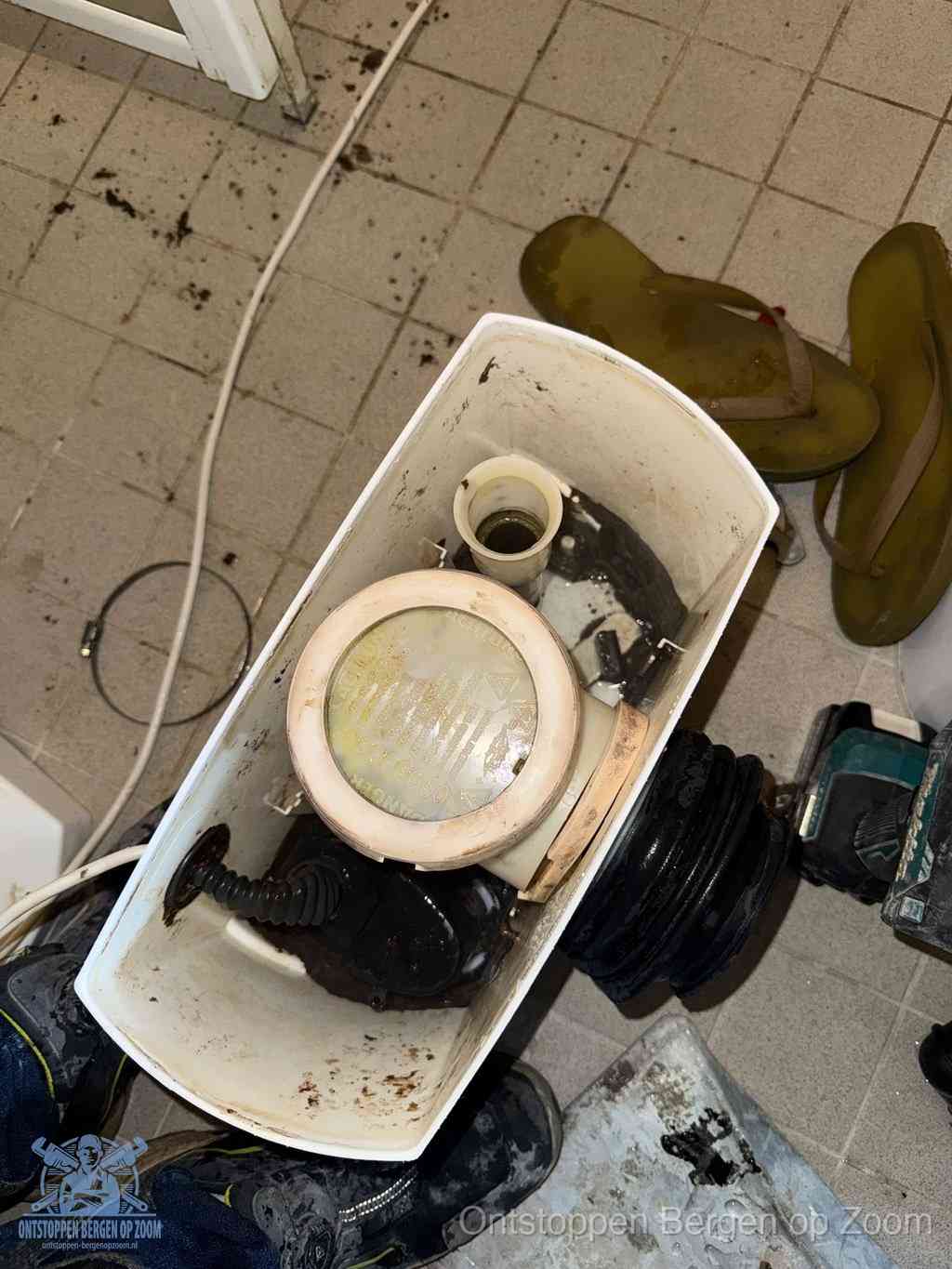 Een gedemonteerde toiletpot op de vloer met ontstoppingsveer en gereedschap ernaast, het verwijderen van een vastzittend voorwerp uit de wc in Bergen op Zoom