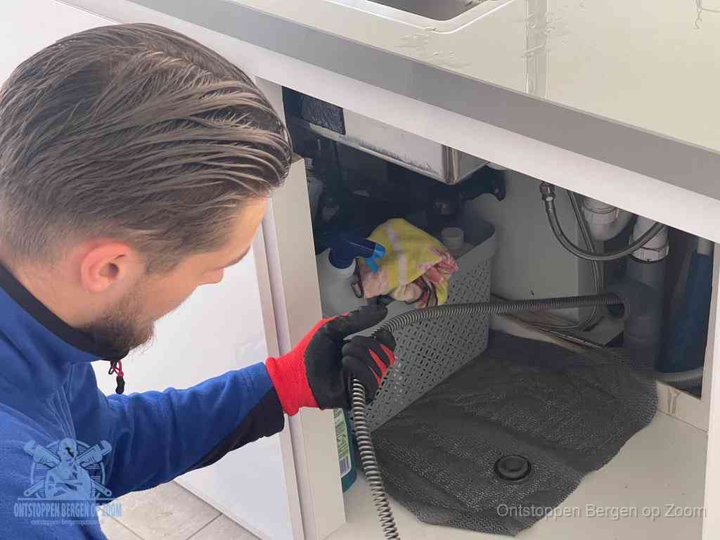 Een monteur voert een flexibele ontstoppingsveer in de afvoer om een verstopping voorbij de bocht van het toilet te bereiken in Bergen op Zoom